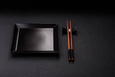 Asya yemekleri için çubuklu boş bir seramik kare siyah tabak. Tasarımınız için yiyecek arkaplanı olarak boş bir kare tabak