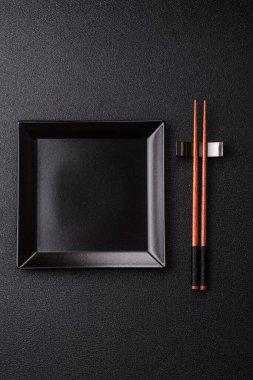 Asya yemekleri için çubuklu boş bir seramik kare siyah tabak. Tasarımınız için yiyecek arkaplanı olarak boş bir kare tabak