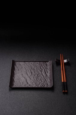 Asya yemekleri için çubuklu boş bir seramik kare siyah tabak. Tasarımınız için yiyecek arkaplanı olarak boş bir kare tabak