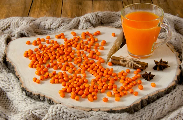 Sea buckthorn fruit drink in a glass, sea buckthorn berries, anise and cinnamon on a wooden background. Knitted scarf around the perimeter. Ingredients for a healthy vitamin drink