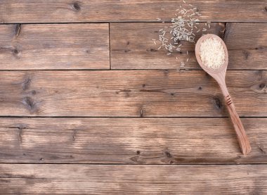 Tahta bir kaşıkta çiğ beyaz pirinç, ahşap bir masada, fotokopi alanı olan üst manzara..