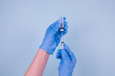 Yeni koronavirüse karşı aşı. Mavi eldivenli bir doktor mavi arka plandaki bir şişeden Coronavirüs aşısı ilacını şırıngaya çeviriyor..