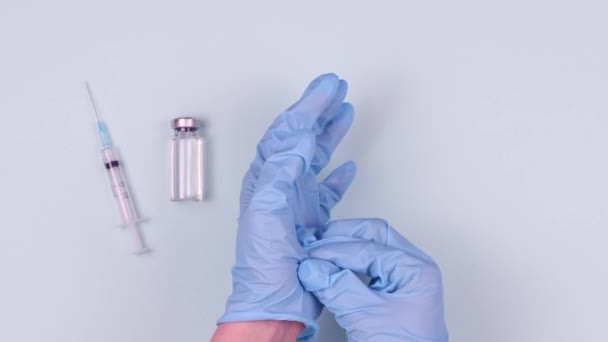 医者は青い手袋を脱ぐ 青い背景にウイルス薬と注射器のボトル 新しいコロナウイルスに対するワクチン接種のアイデア — ストック動画