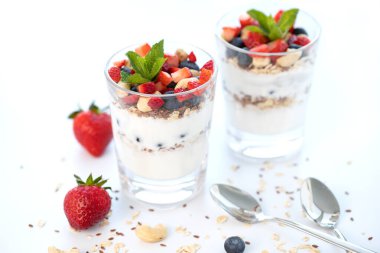 Taze meyve, yoğurt, yabanmersini, keten tohumu ve müsli ile yapılmış iki bardak çilekli parfe. Beyaz arka plan. Sağlıklı Yeme Konsepti.