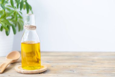 Şişedeki zeytinyağı, bir kaşık ve bir çiçek, beyaz arka plandaki ahşap bir masada. Boşluğu kopyala