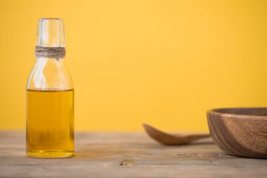 Şişede zeytin yağı, bir kaşık, sarı bir zemin üzerinde ahşap bir masada bir tabak. Boşluğu kopyala