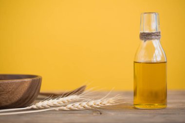 Şişede buğday yağı, buğday kulakları, bir kaşık ve sarı zemin üzerinde ahşap bir masada bir tabak. Boşluğu Kopyala