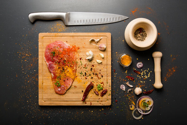 Raw fresh pork meat on board with condiments on dark background
