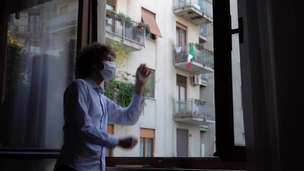 ヨーロッパ イタリア ミラノ マスクで隔離された自宅で40歳の男は パンデミック時に窓の外を見るCovid 19コロナウイルス 流行中のライフスタイル — ストック動画