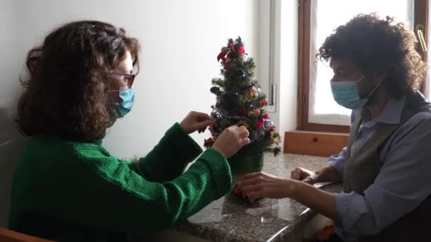 家庭でモミの木を飾る医療マスクのカップル — ストック動画