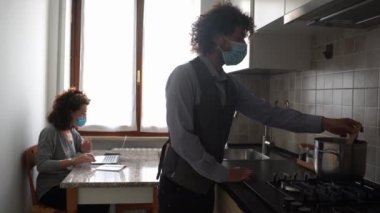 Erkek ve kadın evde tıbbi maskeler takarak yemek pişiriyor..