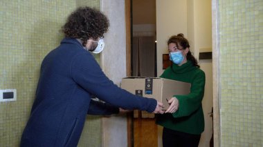 Avrupa, İtalya, Milan Aralık 2020 - Maskeli kadın, Covid-19 Coronavirus 'un kilit altına alındığı sırada evinin kapısındaki dairede Noel için Amazon paketi aldı