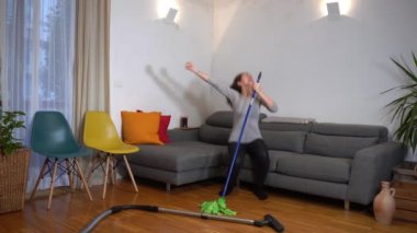 Genç bir kadın, Covid-19 Coronavirus tecridi sırasında temizlik yaparken eğleniyor.