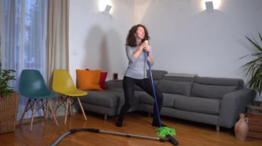 Genç bir kadın, Covid-19 Coronavirus tecridi sırasında temizlik yaparken eğleniyor.