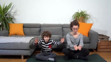 Mutlu ve çılgın aile apartmanda, anne ve oğul Covid-19 Coronavirus karantina evinde yoga meditasyon yapıyorlar - oturma odasında yaşam tarzı