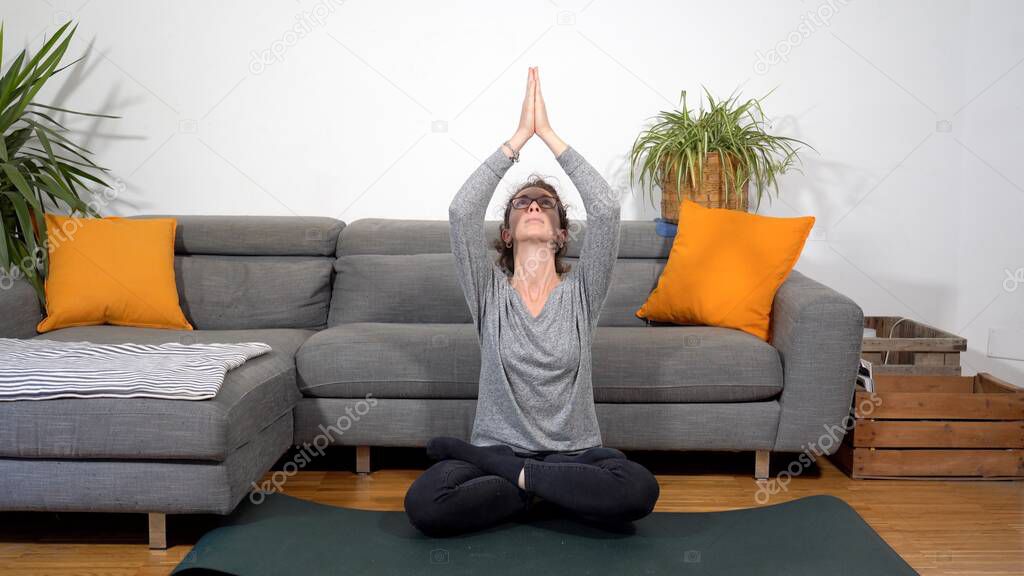 Lady girl 30 years old does yoga meditation  during Covid-19 Coronavirus lockdown quarantine home - lifestyle in living room