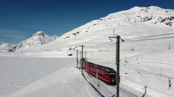 スイスアルプス サンモリッツ2021年2月 ベルニーナ エクスプレス サンモリッツ駅のベルニーナ パスの赤い列車 ユネスコの世界遺産 青空と晴れた日に雪とロシアの鉄道 電車や鉄道の空気の映像 — ストック動画