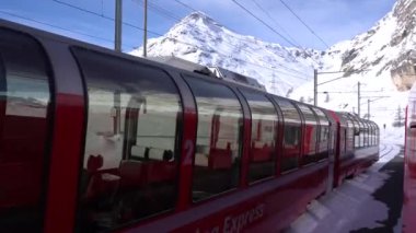 İsviçre Alpleri, Poschiavo Şubat 2021 - Bernina Express 'in insansız hava aracı görüntüsü, Bernina' nın Ospizio Bernina istasyonundaki kırmızı treni - Unesco dünya mirası - Lago Bianco (beyaz göl) 