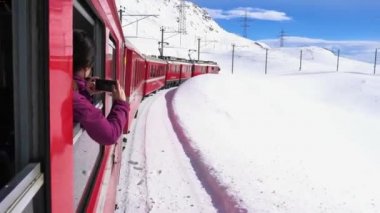 İsviçre Alpleri, Poschiavo Şubat 2021 - Bernina Express 'in insansız hava aracı görüntüsü, Bernina' nın Ospizio Bernina istasyonundaki kırmızı treni - Unesco dünya mirası - Lago Bianco (beyaz göl) 