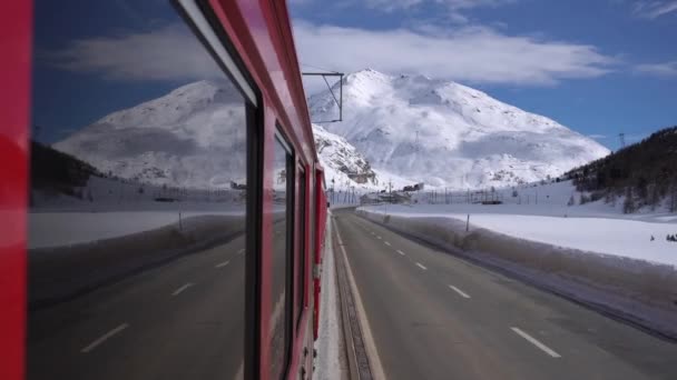 スイスアルプス サンモリッツ2021年2月 ベルニーナ エクスプレス サンモリッツ駅のベルニーナ パスの赤い列車 ユネスコ世界遺産 青空と晴れた日に雪とロシアの鉄道 鉄道の列車からの映像 — ストック動画
