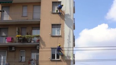 MILAN Nisan 2021 - Yüksek bir binanın şantiyesinde çalışan erkekler. Yüksek irtifa mühendisliği tasarımı için tehlikeli bir iş. Boyama ve dekorasyon binaları. Erkekler evin duvarlarına tırmanıyor.
