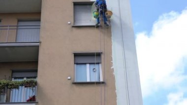 MILAN Nisan 2021 - Yüksek bir binanın şantiyesinde çalışan erkekler. Yüksek irtifa mühendisliği tasarımı için tehlikeli bir iş. Boyama ve dekorasyon binaları. Erkekler evin duvarlarına tırmanıyor.