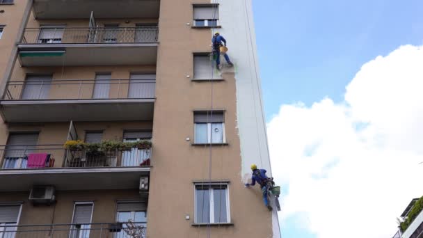 ミラノエイプリル2021 高層ビルの建設現場で働く男性 高高度エンジニアリング設計における危険な作業 絵画や建物を飾る 家の壁を登る男たちは — ストック動画