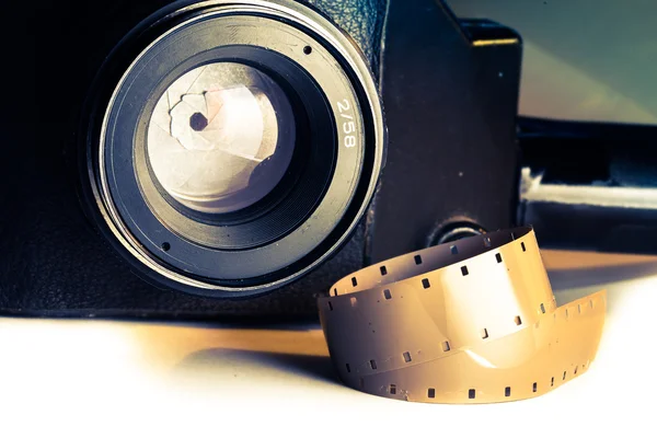 Film strips closeup with vintage movie cinema camera with lens on background — Stock Photo, Image