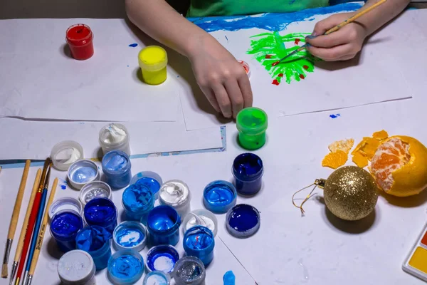 Noel ve Yeni Yıl için resim çizen bir çocuğun elleri boyalı bir masada, bir Altın Noel oyuncağı, bir mandalina veya bir portakal.