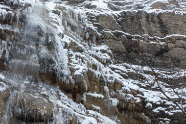 Dağlarda güzel kış manzaraları, ağaçlar, bitkiler, kayalar, şelaleler, sarkıtlar, soğuk havada düşen kar.