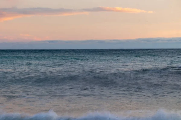 Dalgalı güzel mavi deniz, taşlı sahil, günbatımında gökyüzü