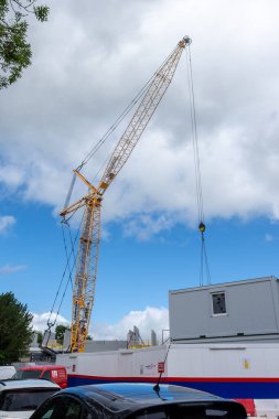 Bir inşaat alanındaki vinç, geçici site ofislerinin arkasındaki eşyaları kaldırırken görüldü. Mavi gökyüzü portre biçiminde bulutlarla kaplıydı.