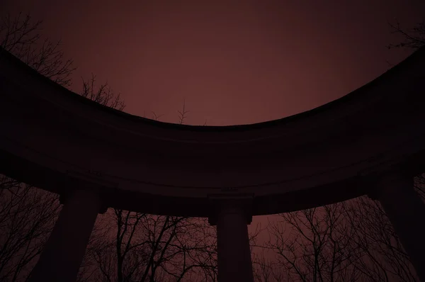 在红光的神秘公园里的老半圆形柱廊 图库照片