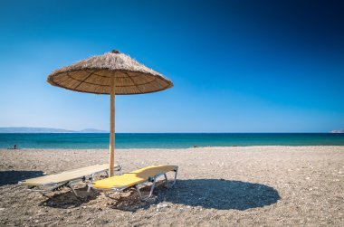 Yunanistan'da bir kum plajındaki saman şemsiye. 