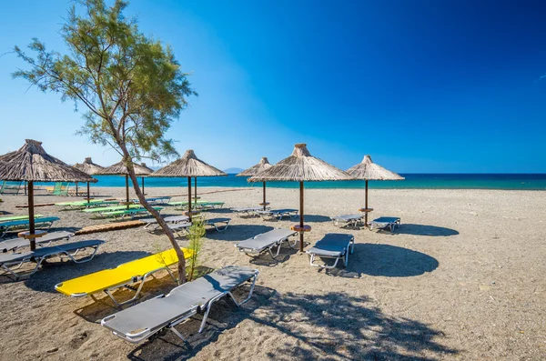 在希腊的沙质海滩上的稻草伞. — 图库照片