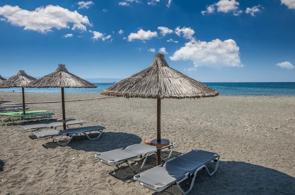 在希腊的沙质海滩上的稻草伞. — 图库照片