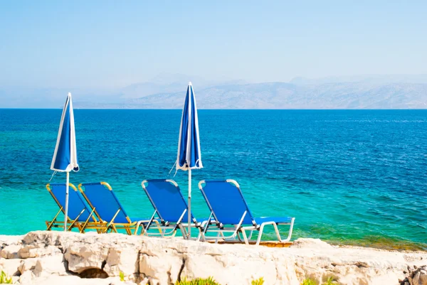 Sunbeds and umbrellas (parasols) on a rocky beach in Corfu Island, Greece — Stock Photo, Image