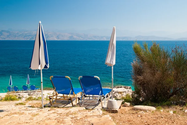 Sunbeds and umbrellas (parasols) on a rocky beach in Corfu Island, Greece — Stock Photo, Image