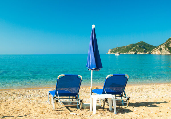 Blue sunbeds and blue umbrella on a beautiful beach in Corfu Island, Greece