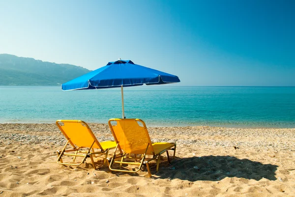 Gele ligbedden en blauw paraplu op een prachtig strand in eiland Corfu, Griekenland — Stockfoto