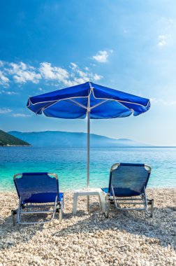 Mavi şemsiye ve bronzlaşma yatak kumsal üzerinde.