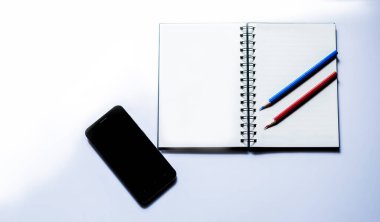 Turuncu arka planda akıllı telefon, kulaklık, defter ve kalem..