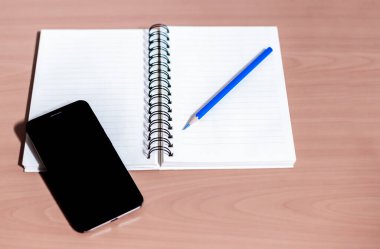 Beyaz arkaplanda akıllı telefon, not defteri ve kalem.