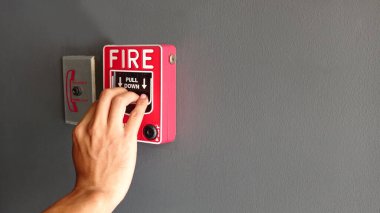 Hand of man pulling fire alarm switch on the white wall as background for emergency case. clipart