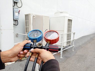 Hava onarım teknisyeni endüstriyel fabrika klimalarını doldurmak ve dış hava kompresörü ünitesini kontrol etmek için ölçüm ekipmanı kullanıyor..