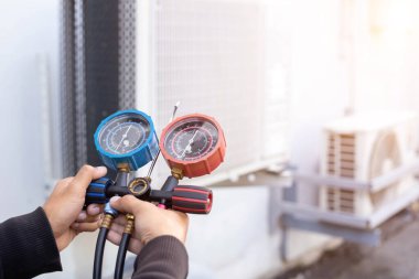 Hava onarım teknisyeni endüstriyel fabrika klimalarını doldurmak ve dış hava kompresörü ünitesini kontrol etmek için ölçüm ekipmanı kullanıyor..