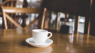 Kahve fincanı ve çay tabağı ahşap bir masada. Koyu arkaplan.