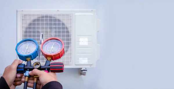 Air repair mechanic using measuring equipment for filling industrial factory air conditioners and checking maintenance outdoor air compressor unit.