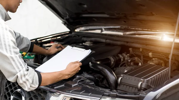 Automobile mechanic repairman checking a car engine with inspecting writing to the clipboard the checklist for repair machine, car service and maintenance.