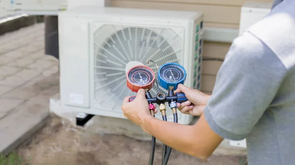 Hava onarım teknisyeni endüstriyel fabrika klimalarını doldurmak ve dış hava kompresörü ünitesini kontrol etmek için ölçüm ekipmanı kullanıyor..